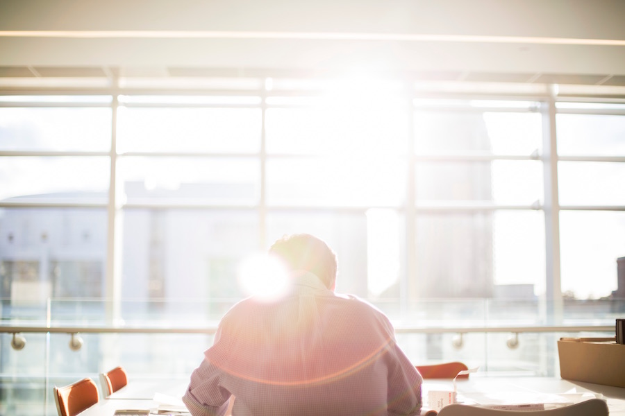 Man hunched over desk working with sunlight streaming through windows